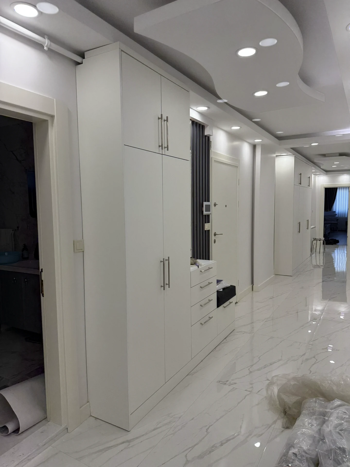 Arnavutköy özel ölçü modern portmanto uygulaması; tavana kadar beyaz dolaplar, siyah dekoratif duvar paneli, LED aydınlatmalı ayna ve minderli oturma alanı.