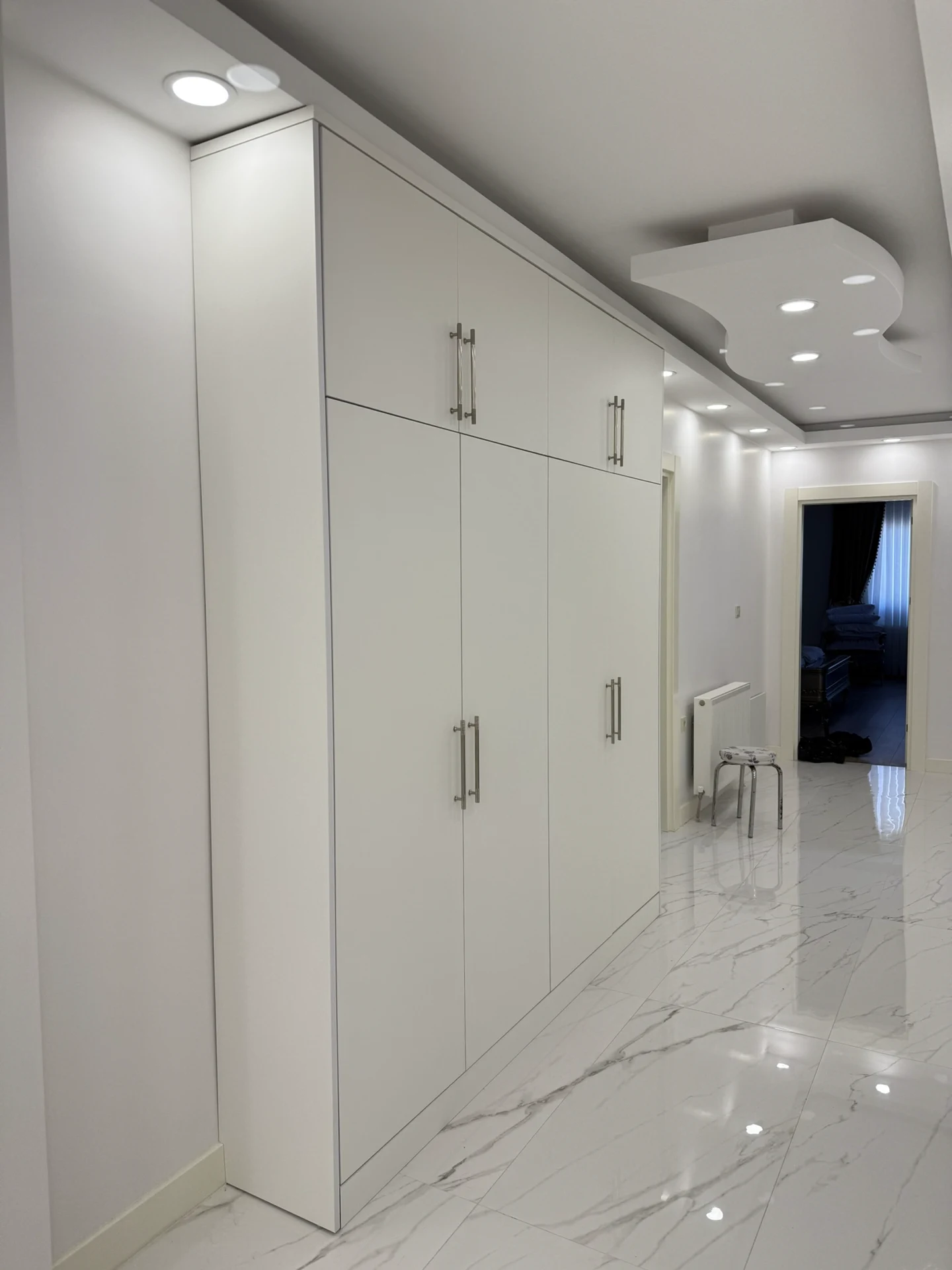Arnavutköy özel ölçü modern portmanto uygulaması; tavana kadar beyaz dolaplar, siyah dekoratif duvar paneli, LED aydınlatmalı ayna ve minderli oturma alanı.