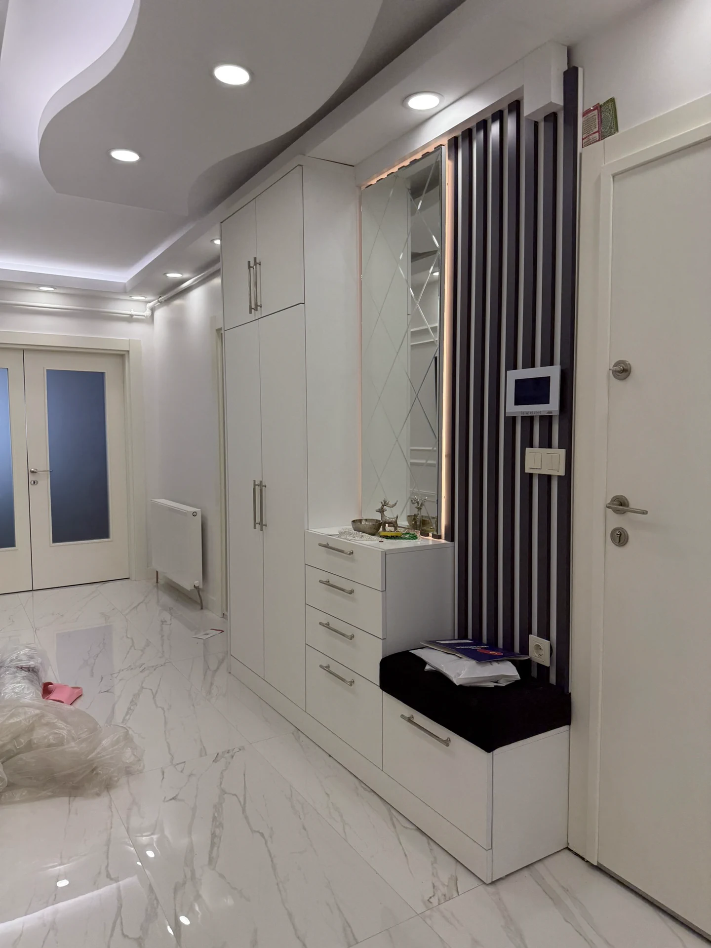 Arnavutköy özel ölçü modern portmanto uygulaması; tavana kadar beyaz dolaplar, siyah dekoratif duvar paneli, LED aydınlatmalı ayna ve minderli oturma alanı.